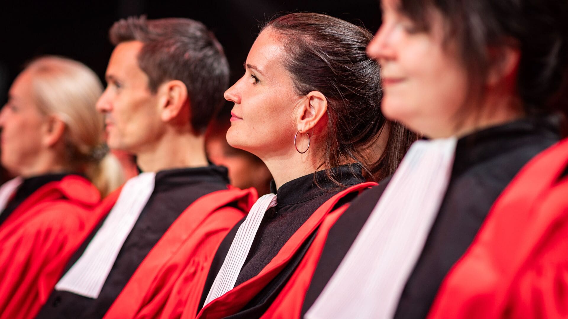 Several people dressed in red robes and black ties, gathered closely in a formal environment.